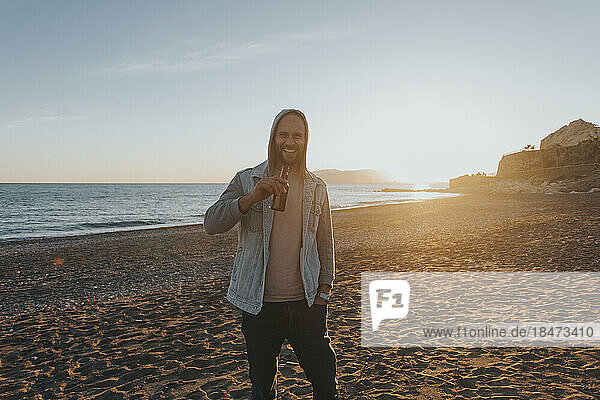 Happy man standing with bottle of beer at beach