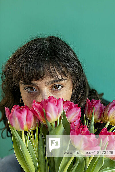 Woman covering face with tulips against green background