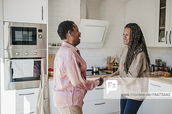 Happy woman dancing with mother in kitchen at home