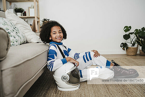 Smiling girl wearing space suit sitting near sofa at home