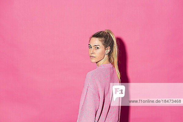 Blond woman standing against pink background