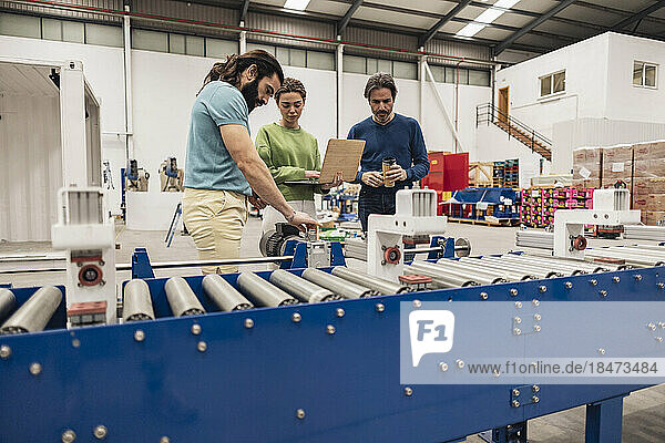 Engineers examining machine parts standing by conveyor belt in factory