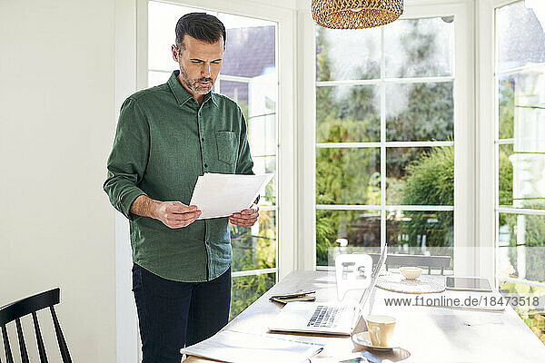 Thoughtful man reading documents standing by desk