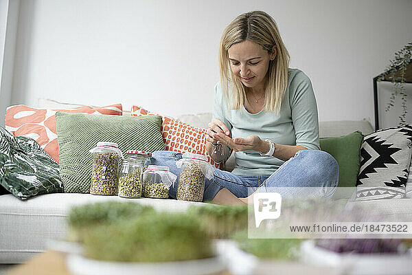 Woman with various beans sprout jars on sofa at home