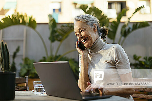 Happy freelancer talking on smart phone sitting in back yard
