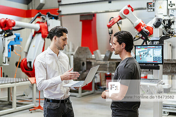 Colleague explaining technician through laptop in robot factory