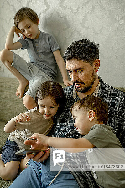 Father and sharing smart phone with kids on sofa at home
