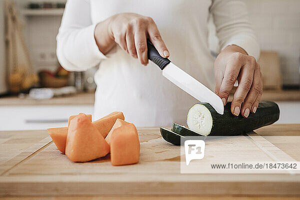 Woman with kitchen knife cutting cucumber at home