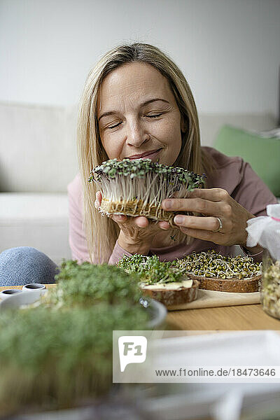 Smiling woman with eyes closed smelling homegrown herbs at home