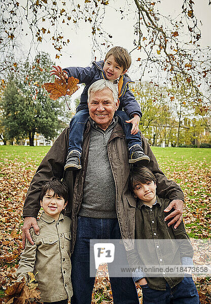 Smiling senior man standing with grandsons at park
