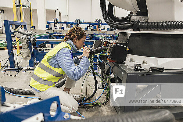 Ingenieur trägt reflektierende Kleidung und analysiert Maschinenteile mit Taschenlampe in der Fabrik