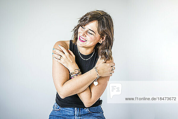 Happy woman hugging herself in front of white wall