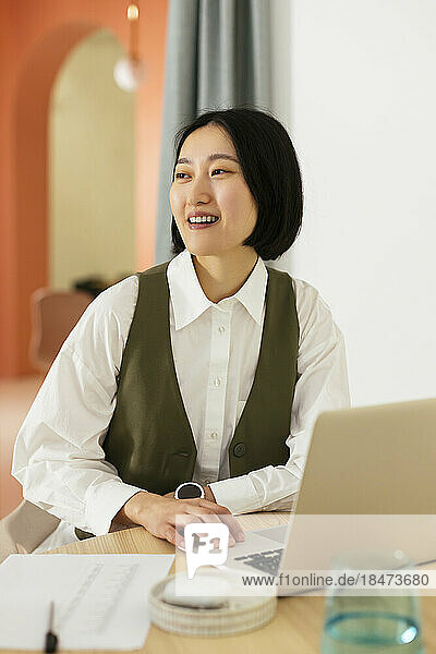 Glückliche Geschäftsfrau mit kurzen Haaren sitzt am Schreibtisch im Büro