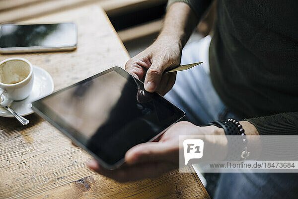 Hands of man using tablet PC on table in cafe