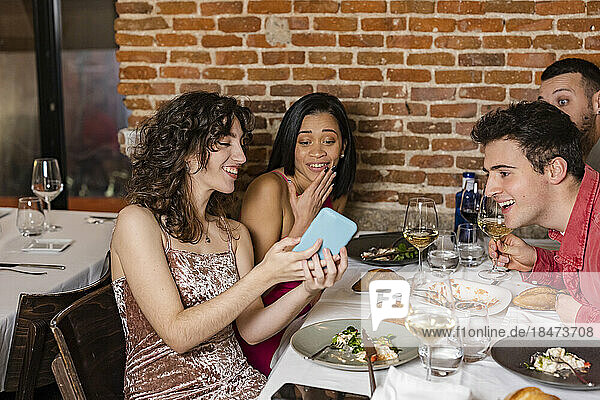 Happy woman sharing smart phone with friends at restaurant