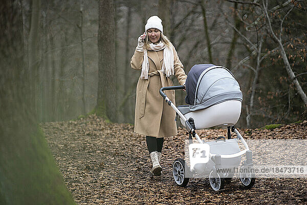 Woman with baby stroller talking on smart phone in forest