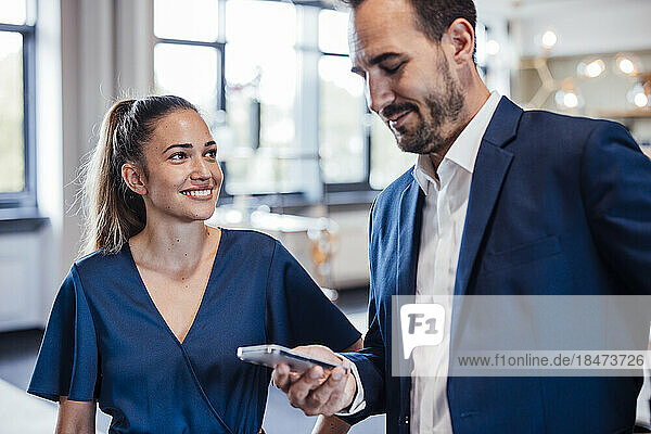 Businessman using mobile phone with colleague standing at office