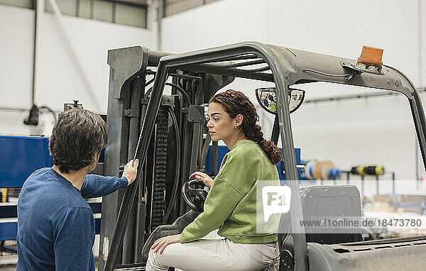 Engineer sitting in forklift discussing with colleague at factory