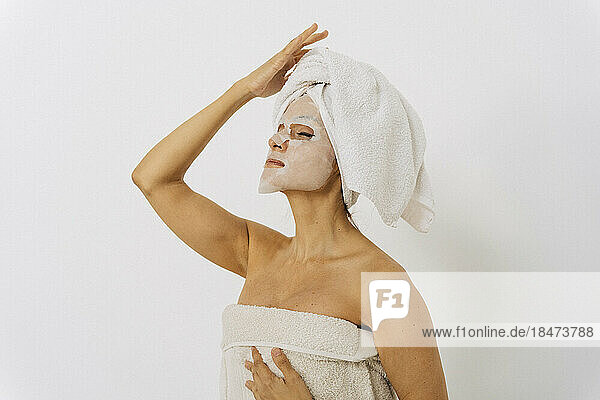 Woman wearing facial sheet mask standing in front of white wall