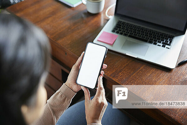 Hands of businesswoman holding smart phone with blank screen at loft office