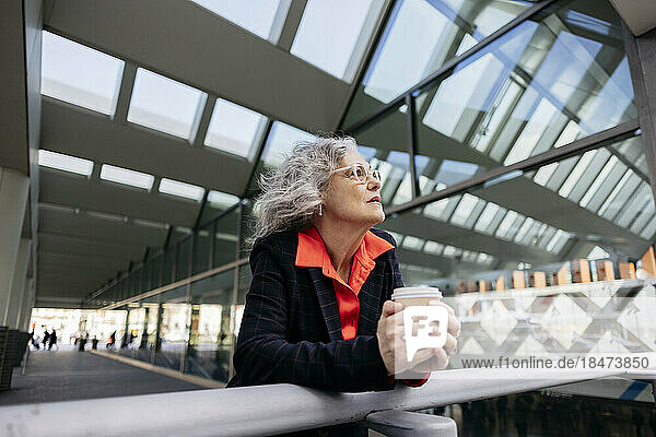 Thoughtful mature businesswoman with disposable cup leaning on railing
