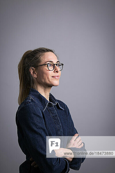 Thoughtful mature businesswoman wearing eyeglasses against gray background