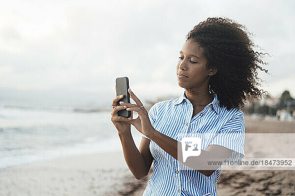 Young woman photographing through smart phone at beach