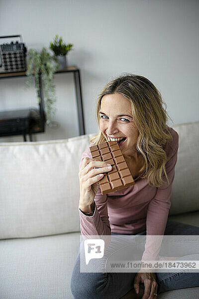 Happy woman eating chocolate on sofa at home