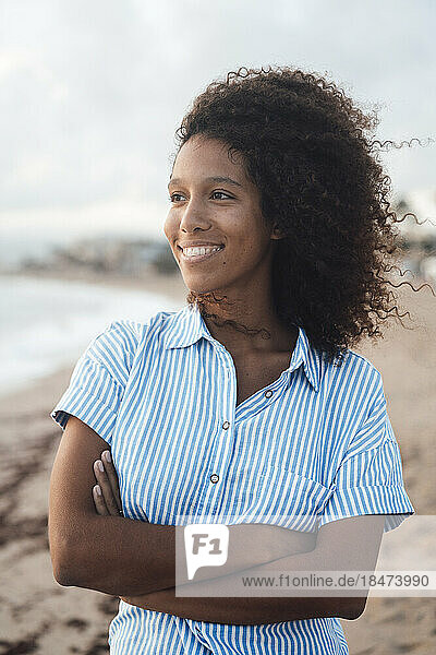 Happy woman with arms crossed standing on coastline at beach