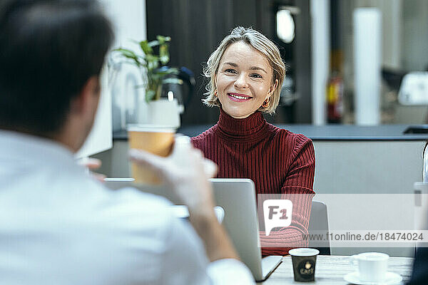 Smiling businesswoman discussing with colleague at desk