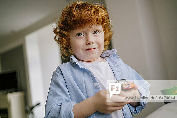 Redhead boy holding toy car in hand at home