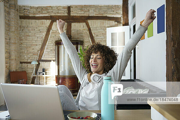 Happy freelancer cheering in front of laptop at home