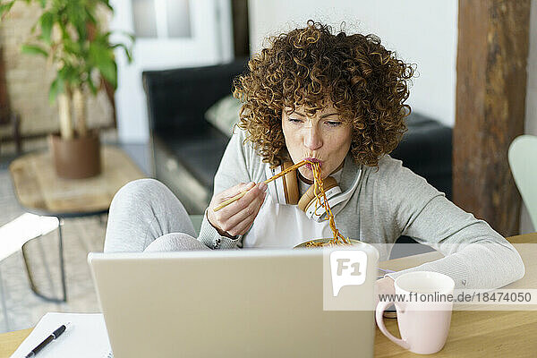 Freelancer eating noodles and working on laptop at home