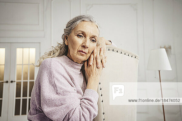 Contemplative senior woman with gray hair sitting on chair at home