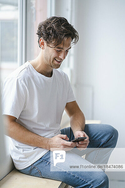 Happy young man using smart phone by window