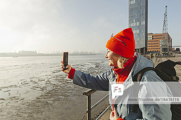 Frau fotografiert Fluss mit Smartphone