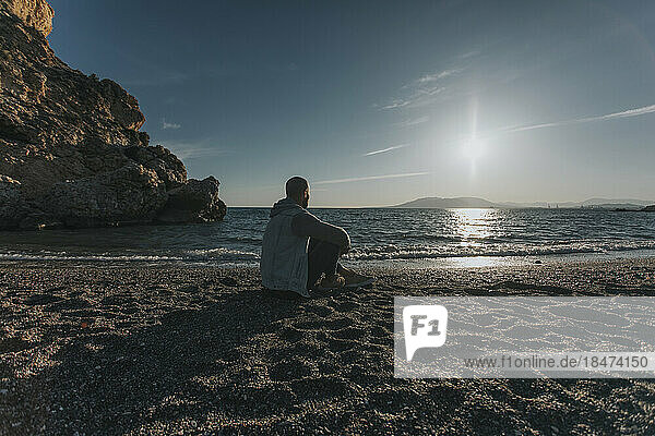 Nachdenklicher Mann sitzt bei Sonnenuntergang am Strand