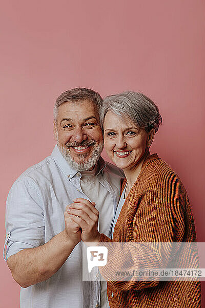 Smiling mature couple standing together against pink background