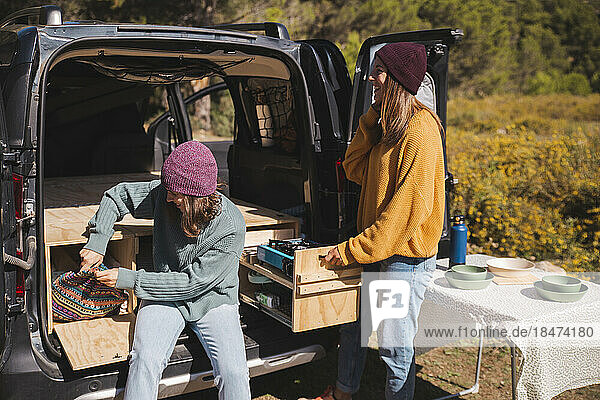 Smiling friends unloading wooden boxes form trunk of campervan