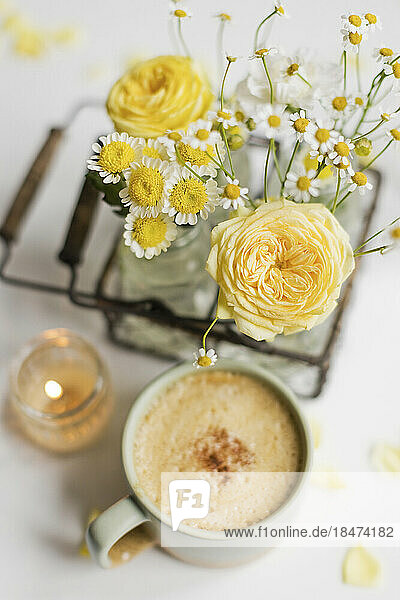 Cup of coffee by yellow and white flowers on table
