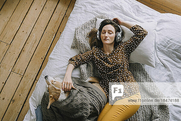 Carefree woman listening to music through headphones lying on bed at home