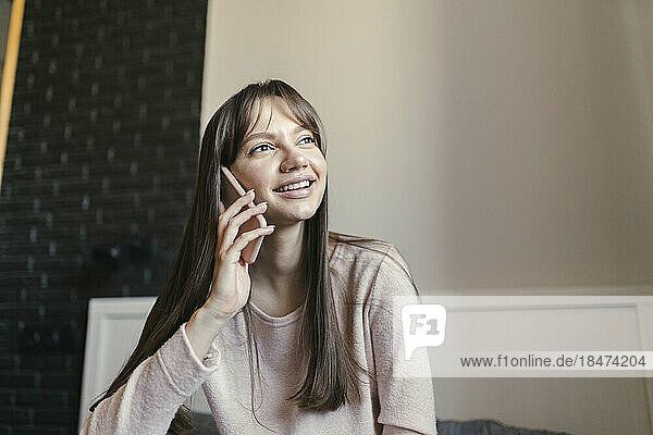 Smiling young woman talking on smart phone in bedroom at home