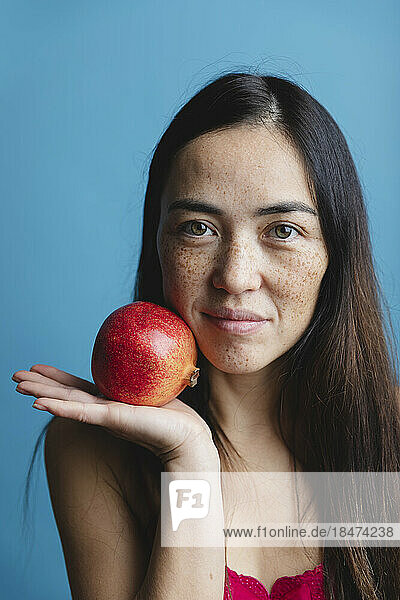 Smiling woman holding pomegranate fruit against blue background
