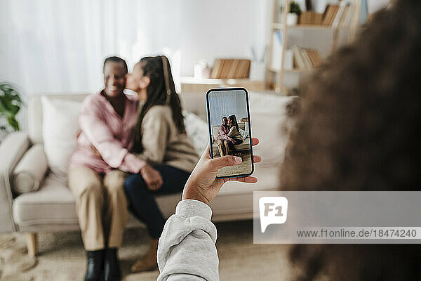 Girl photographing mother and grandmother through smart phone at home