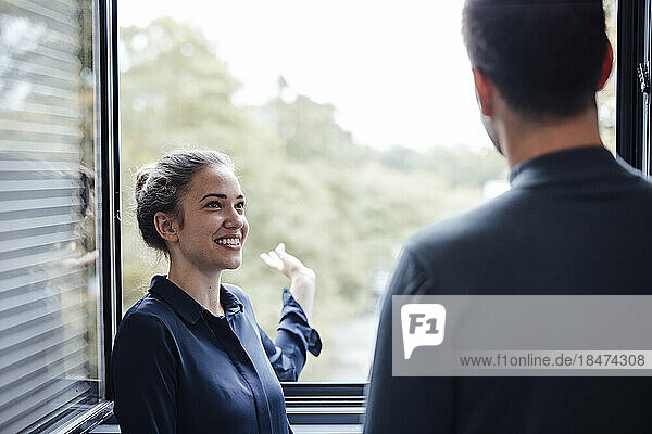 Smiling young businesswoman discussing with colleague by window