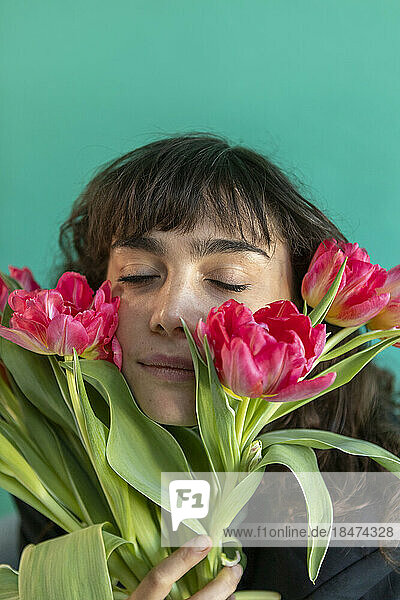 Woman with eyes closed holding tulips against green background