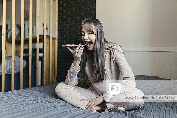 Happy woman talking on speaker phone at bedroom