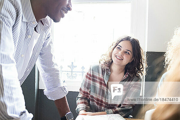 Happy businesswoman looking at colleague discussing strategy in office