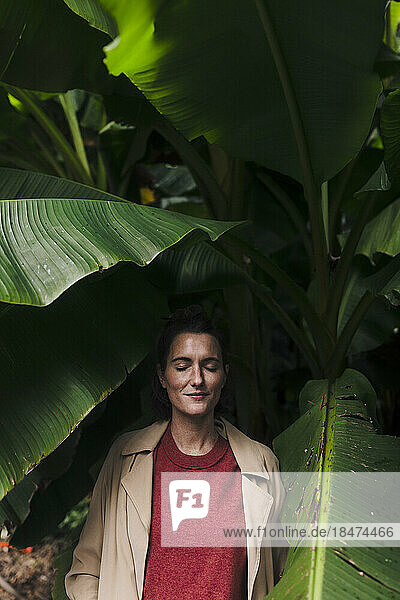 Smiling woman standing under banana leaves