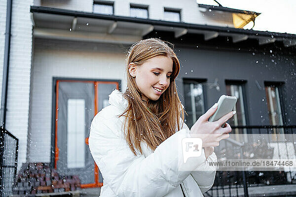 Happy teenage girl text messaging through smart phone outside home